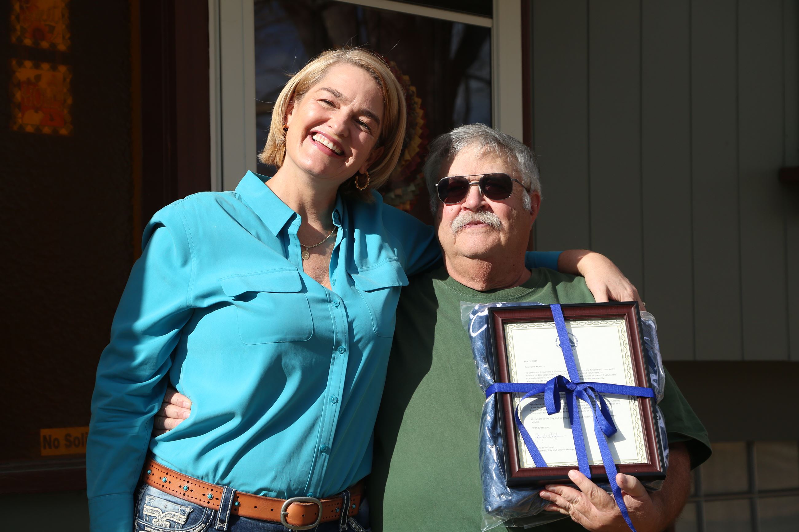 City Manager stands with volunteer holding framed letter and smiling for the camera
