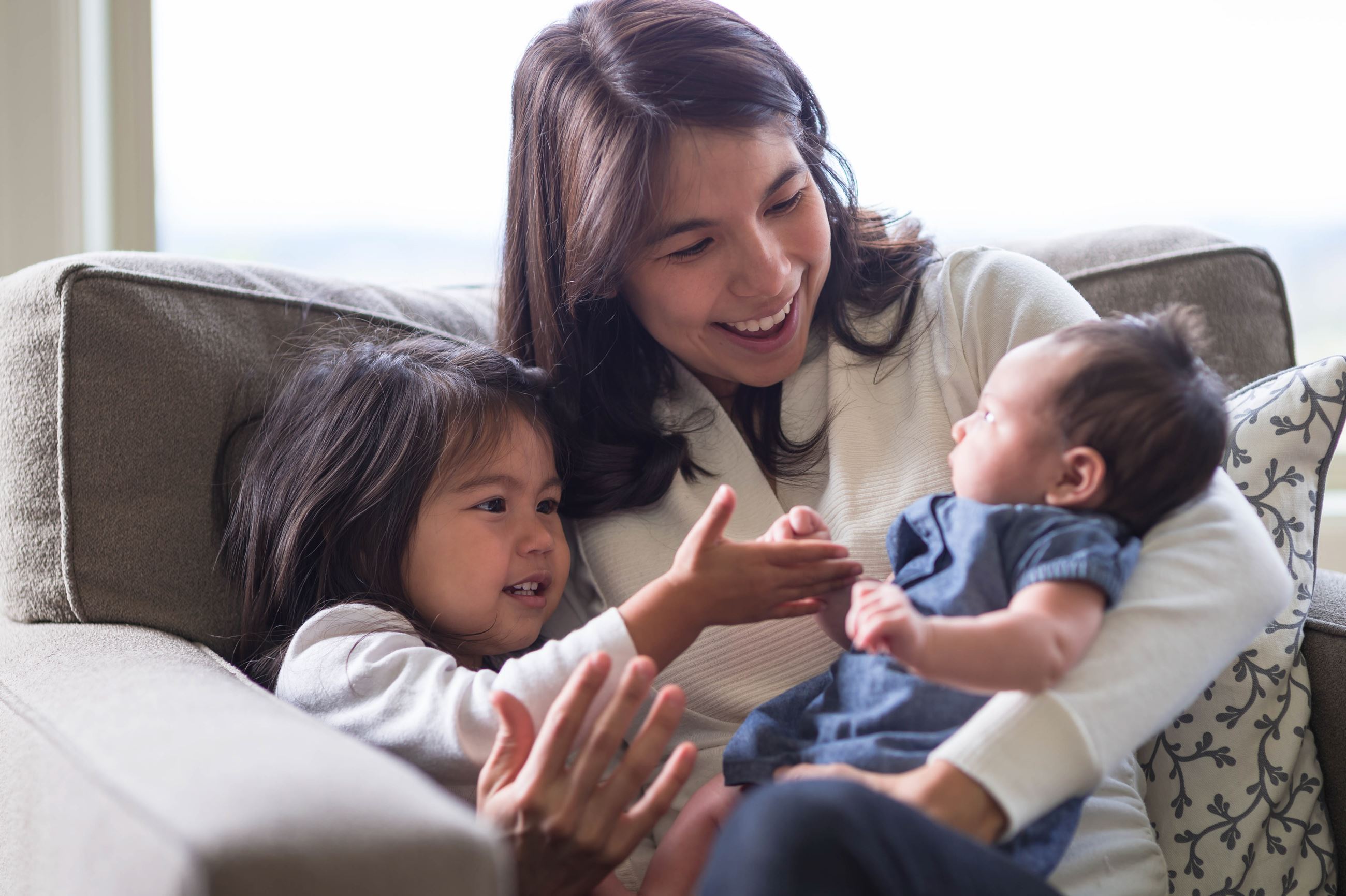 Family sitting on couch together - parent holding newborn and sibling
