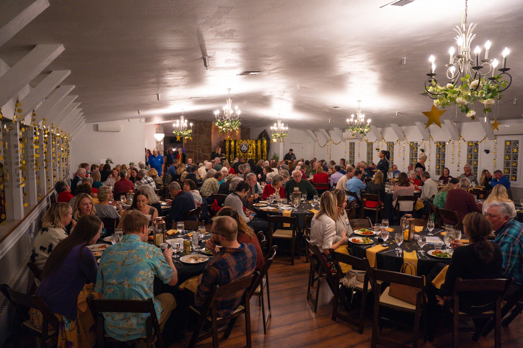 Volunteers eating dinner at the event venue. Round tables with black tablecloths and gold napkins.